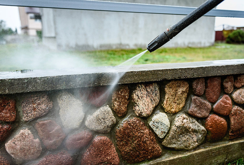 Cleaning dirty stone fence using high pressure power washer. Effektive Reinigungslösungen: Hochdruckreiniger im Einsatz zur Fassaden- und Oberflächenreinigung